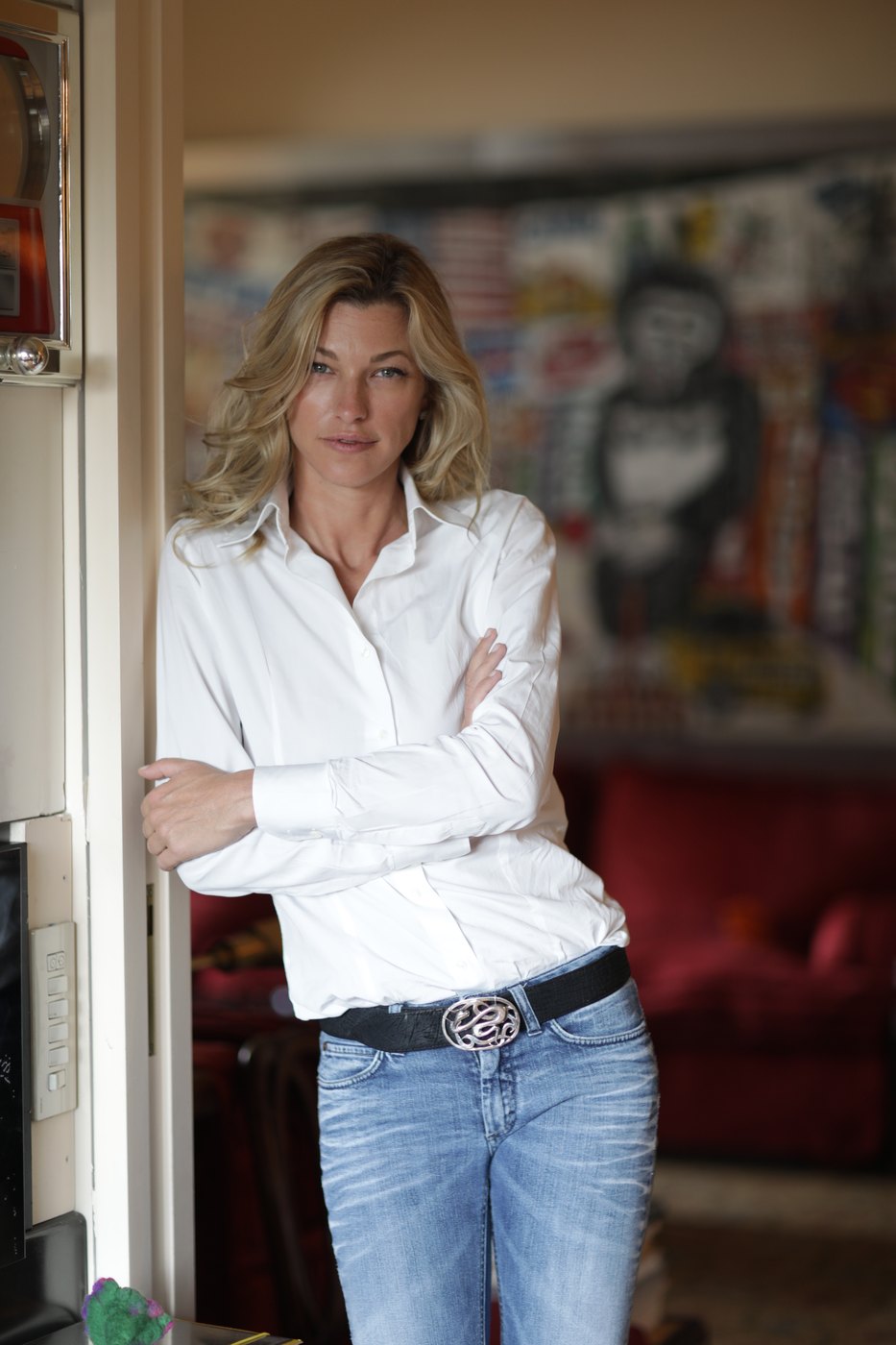 Nicole Junkerman in camicia bianca sulla soglia di una stanza luminosa, con opere colorate alle pareti